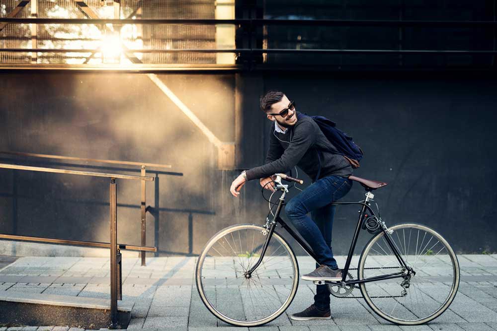 En leende man står med sin cykel och vänder sig om för att titta bakåt