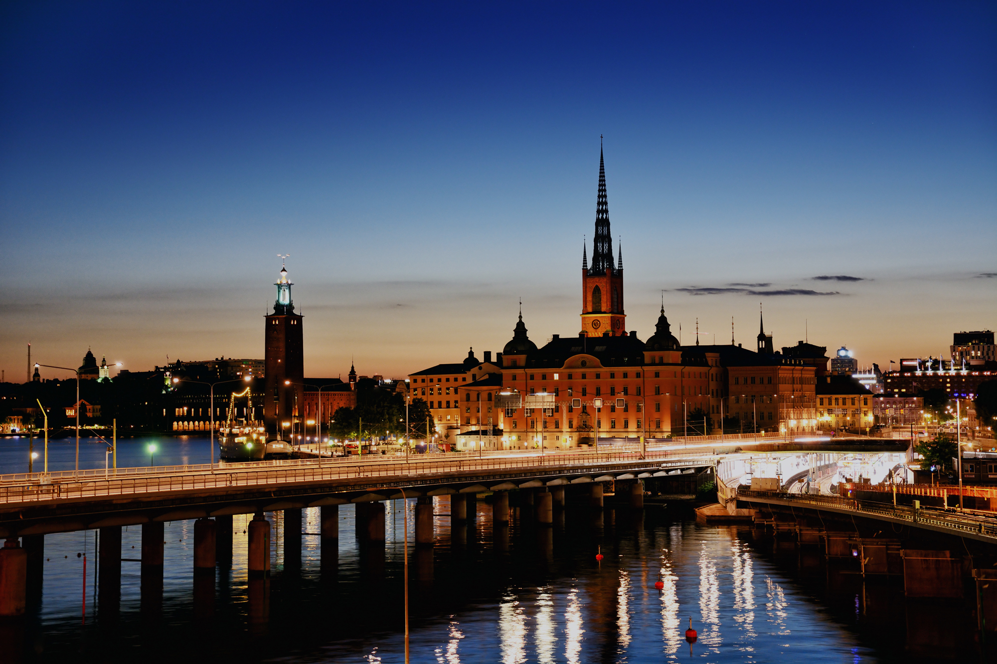 Kvällsbild över Riddarholmen där byggnader, vägar och omgivande vatten lyses upp av stadens belysning